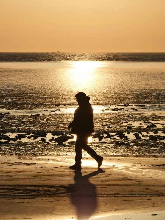 a person walking along a beach in front of the sun