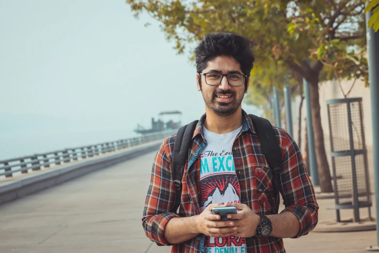 a man wearing glasses and a tee shirt is holding a cell phone