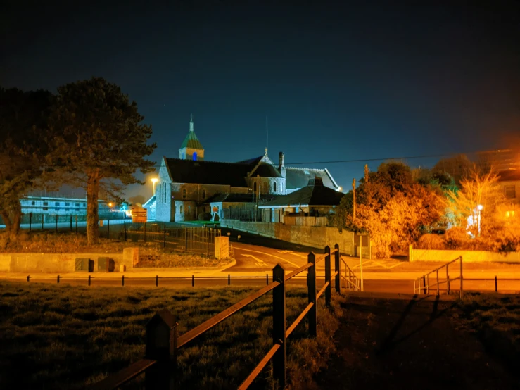 some buildings lights trees grass and a fence