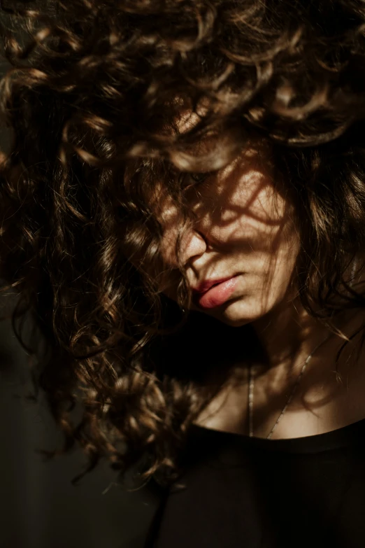 a woman with long curly hair has its head tilted down