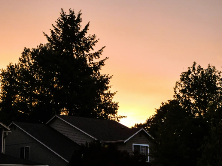 the house is next to the trees and a sunset