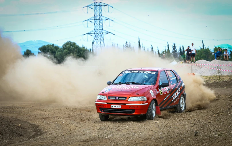 a red car driving in sand near a field