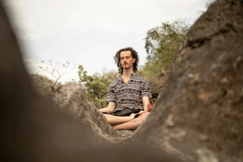 a man sitting in a lotus position by some rocks