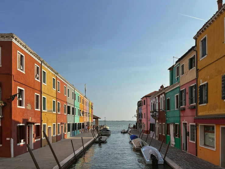 a canal with boats parked near buildings and people walking on the sidewalk