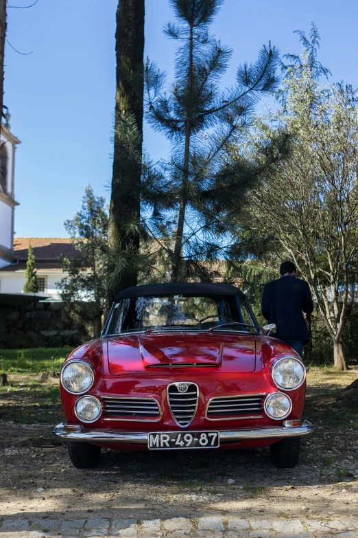 a man is standing beside a red old fashioned car