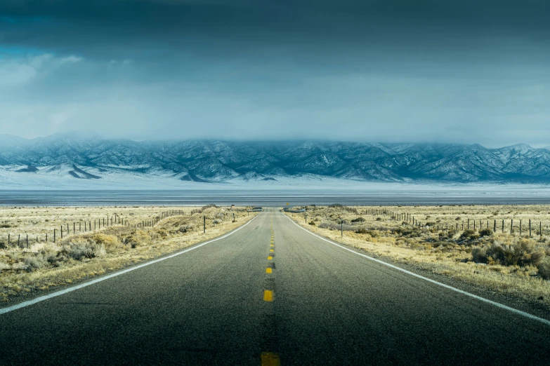 an empty highway in a desert with a mountain range in the background