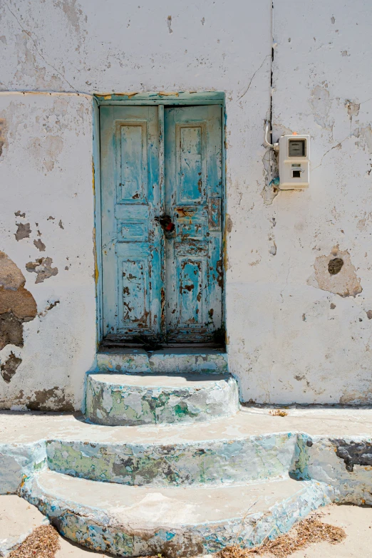 a weathered building with a rusted blue door and set of stone steps