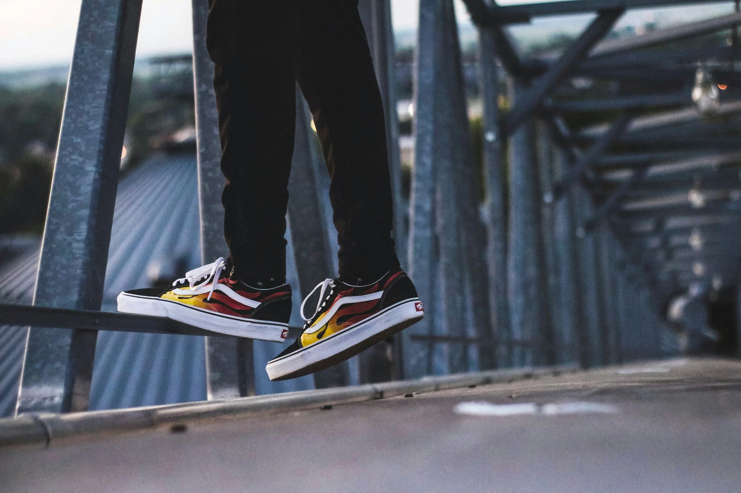 a person wearing black, yellow and red vans shoes is standing on the edge of a metal railing