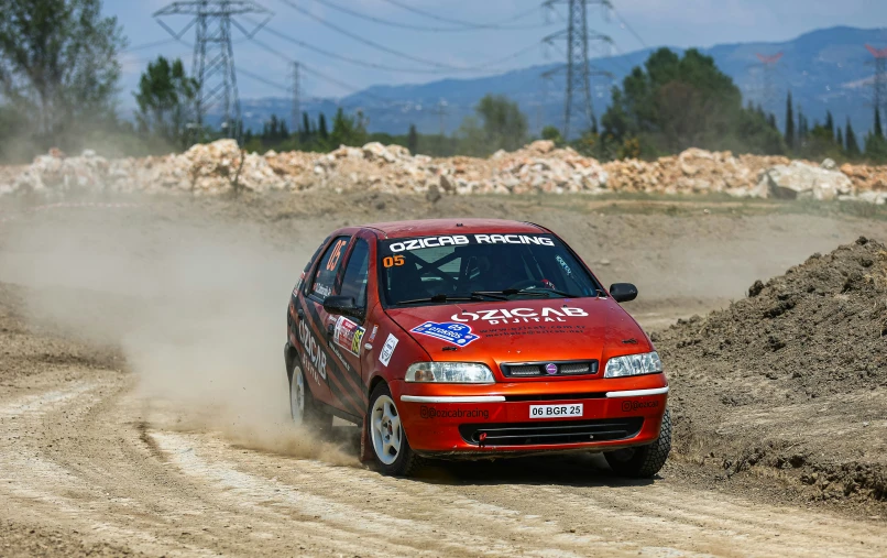 red car driving through dirt field with sky in background