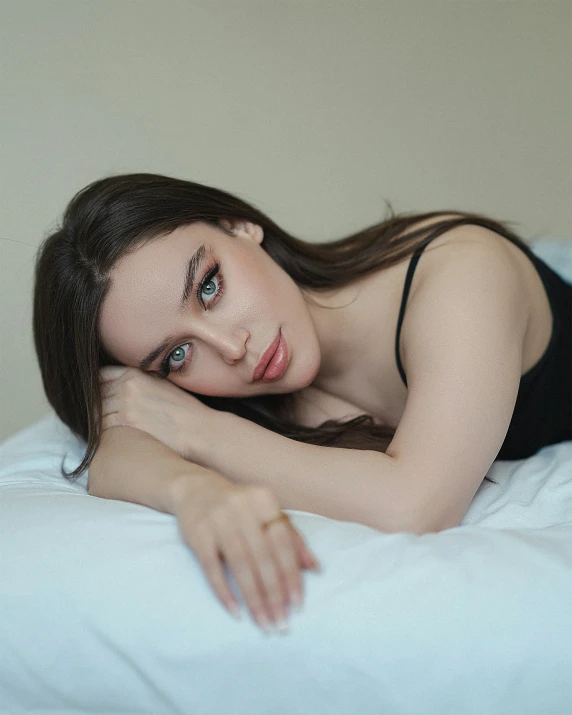 a beautiful young woman in a black top laying on a bed