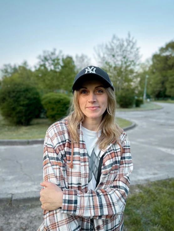 a woman in a hat with her arms crossed standing in front of an empty road