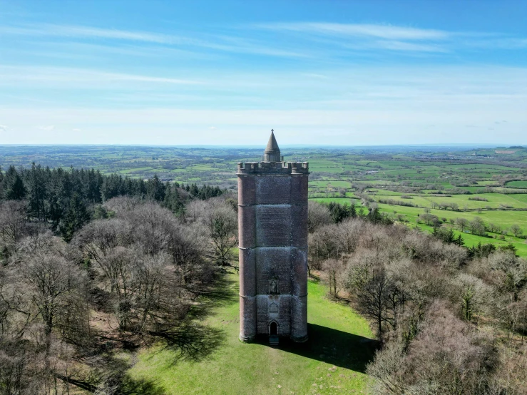 a tower sits in a large grassy area surrounded by trees