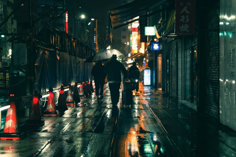 a night time view of people holding umbrellas, walking down a city street