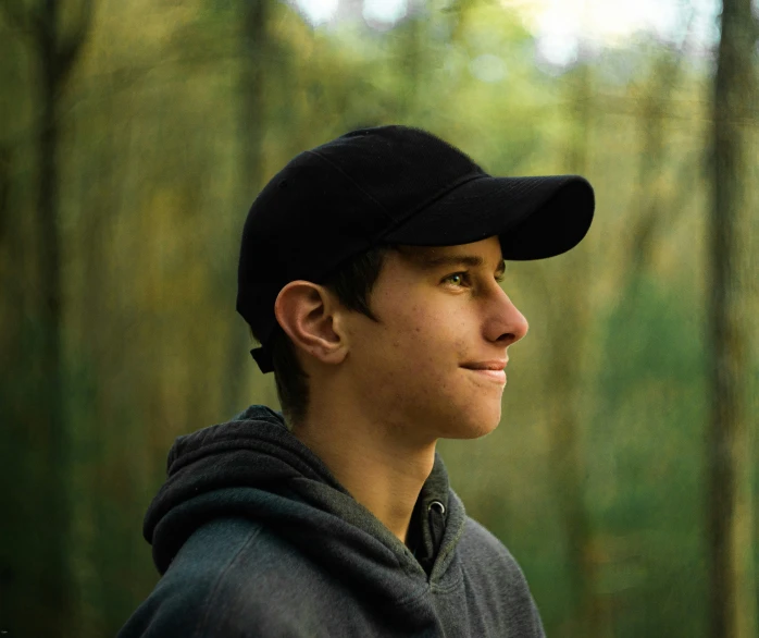 a boy wearing a baseball hat standing in front of trees