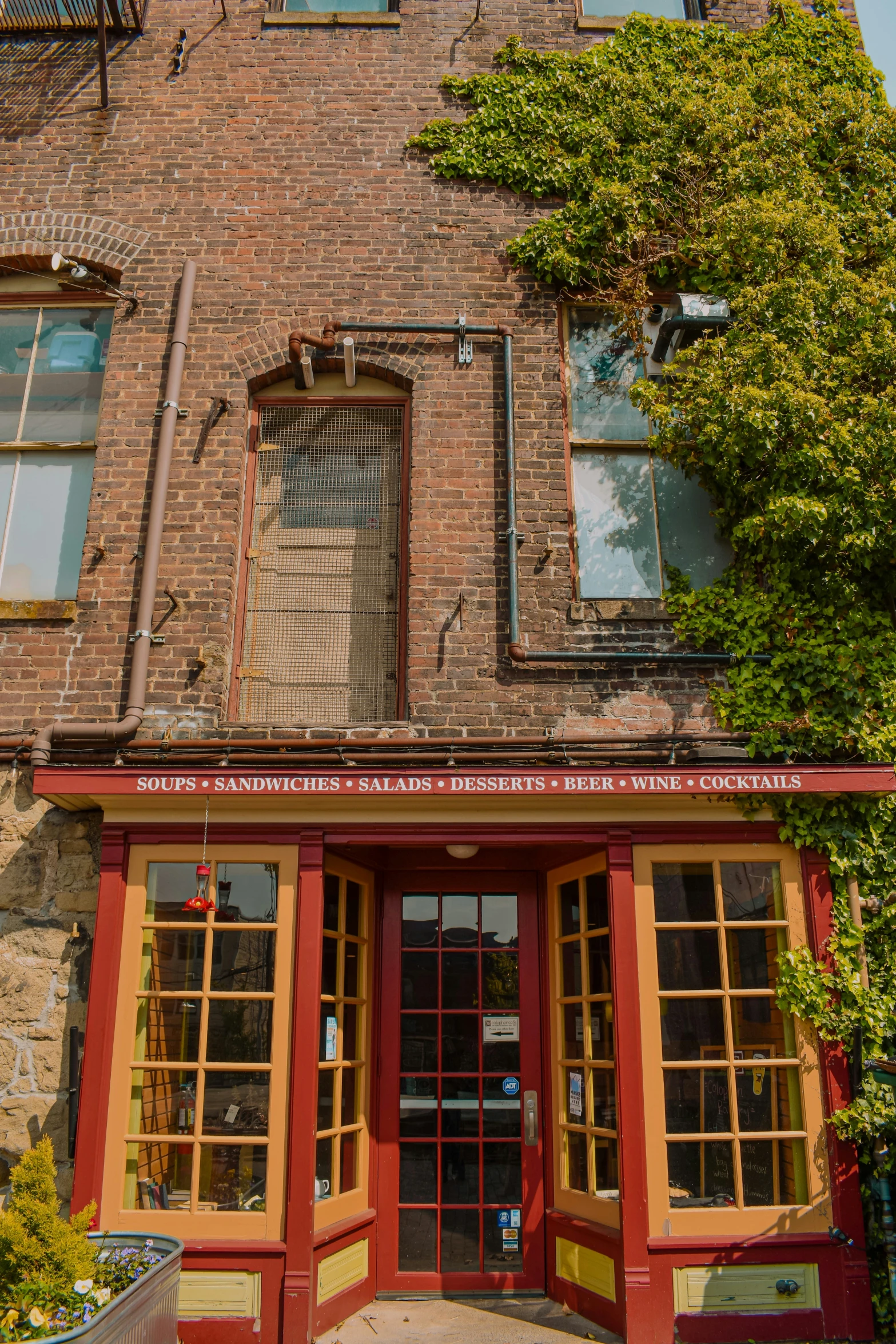 a brick building with double doors, windows and lots of greenery