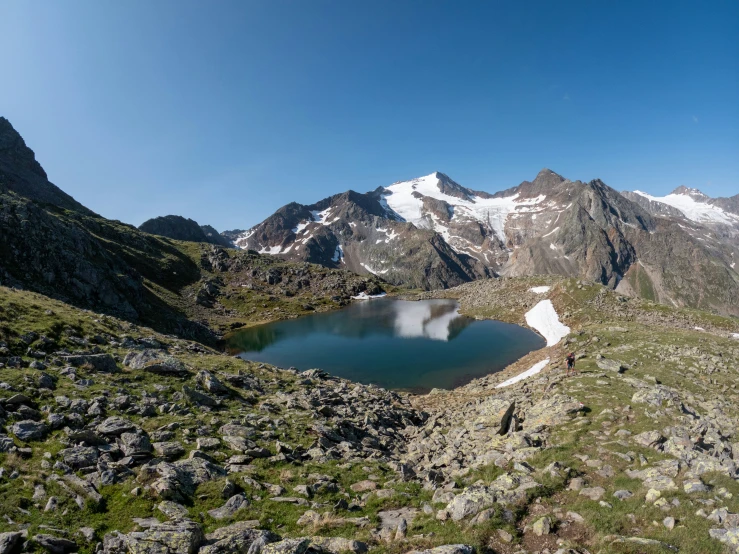 a mountain landscape with snow - capped peaks, and a large lake surrounded by rocks