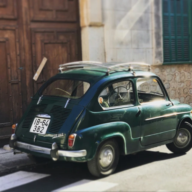 a green vintage car with a surfboard on top parked in a side street