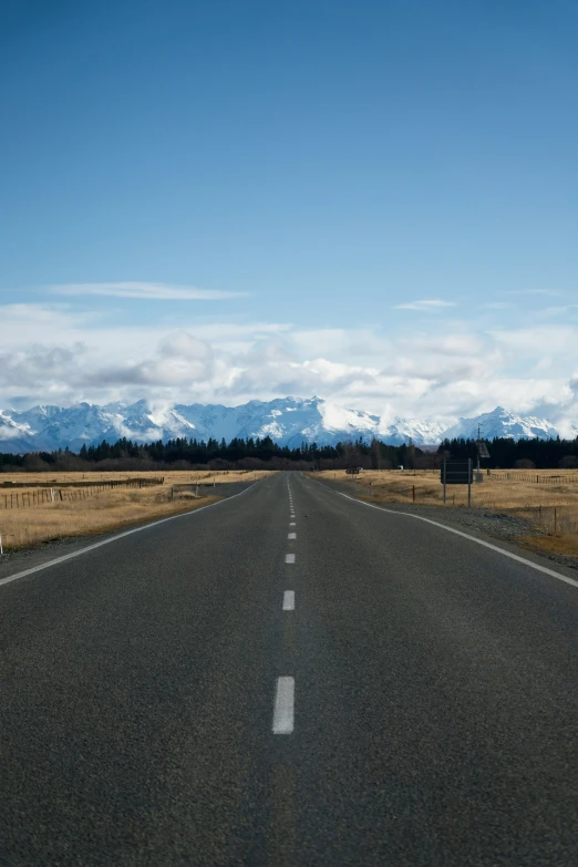 a long stretch of road with snow capped mountains in the distance