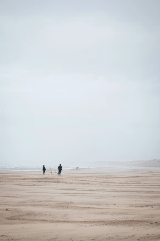 two people walk on the beach in heavy wind