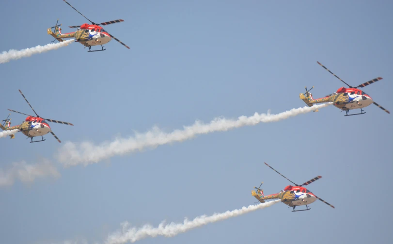 four aircraft flying through a blue sky leaving smoke behind them