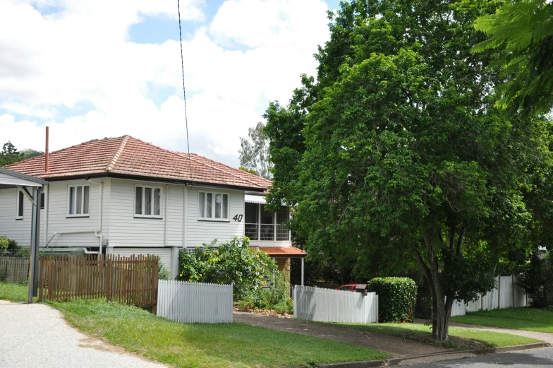 a two story house sitting on the corner of a road with a large tree