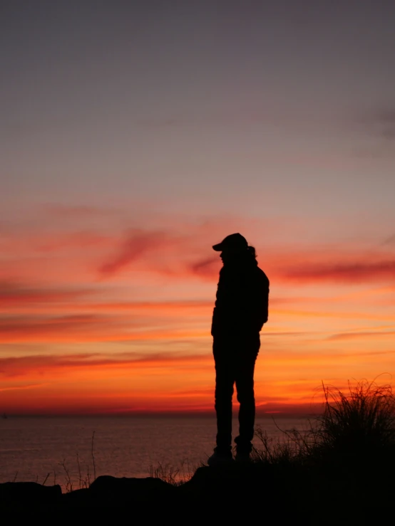 silhouetted man looking at sunset over body of water