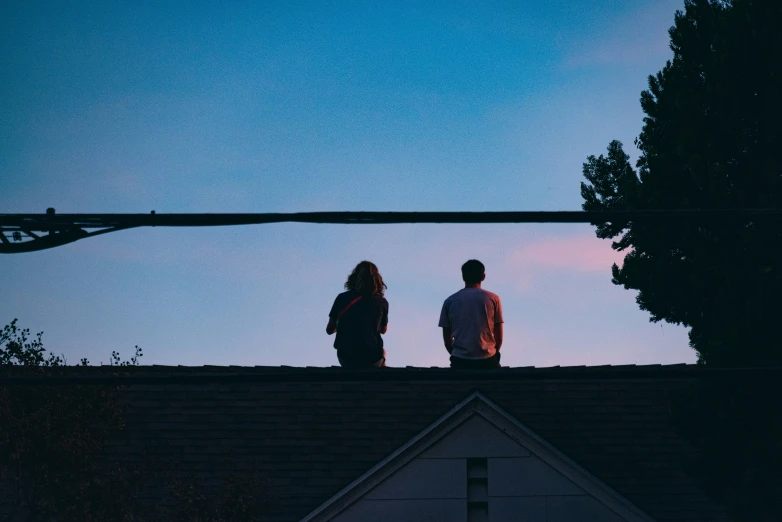 two people sitting on the top of a roof watching the sunset