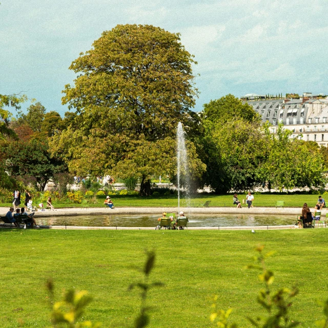 a group of people sit around an outdoor fountain in a park