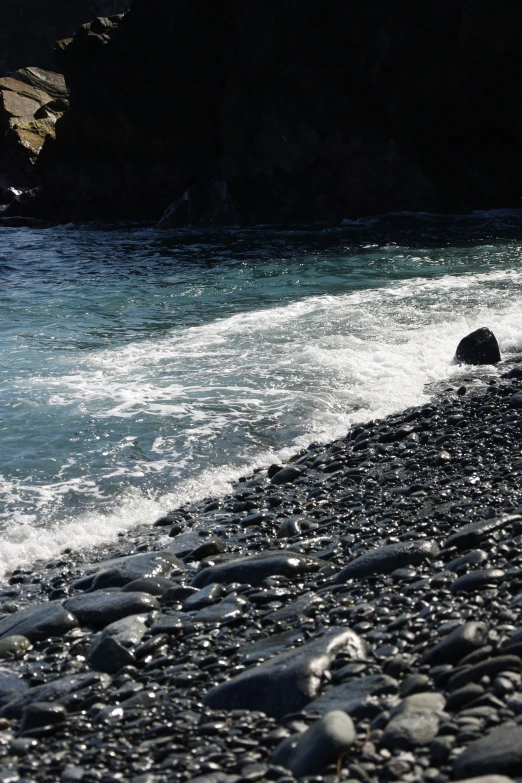 a rocky beach with a man walking towards the water