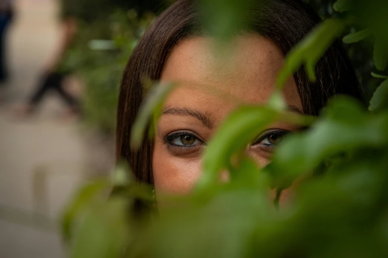 a girl stares through some leaves in the foreground