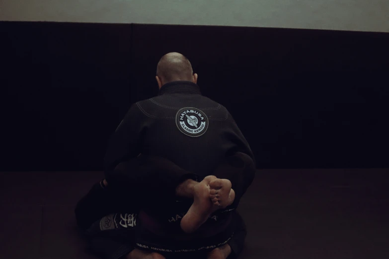 the back view of an athlete sitting on the ground wearing a black uniform and a bald head