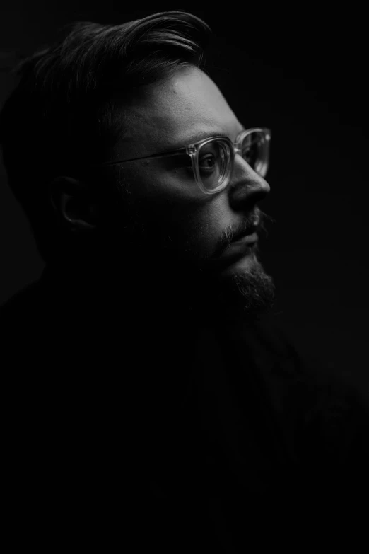 man wearing glasses in dark room with a beard