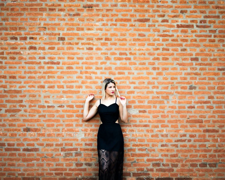 a woman in black clothing standing near a brick wall