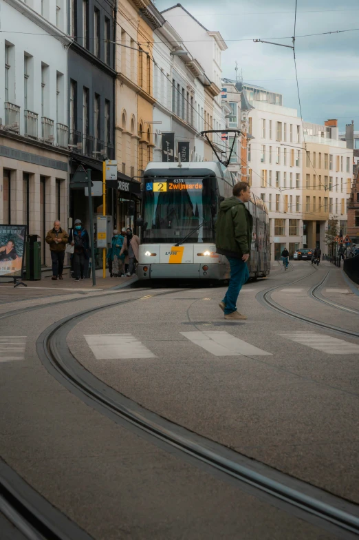 people stand on the edge of a city street while a tram rolls by