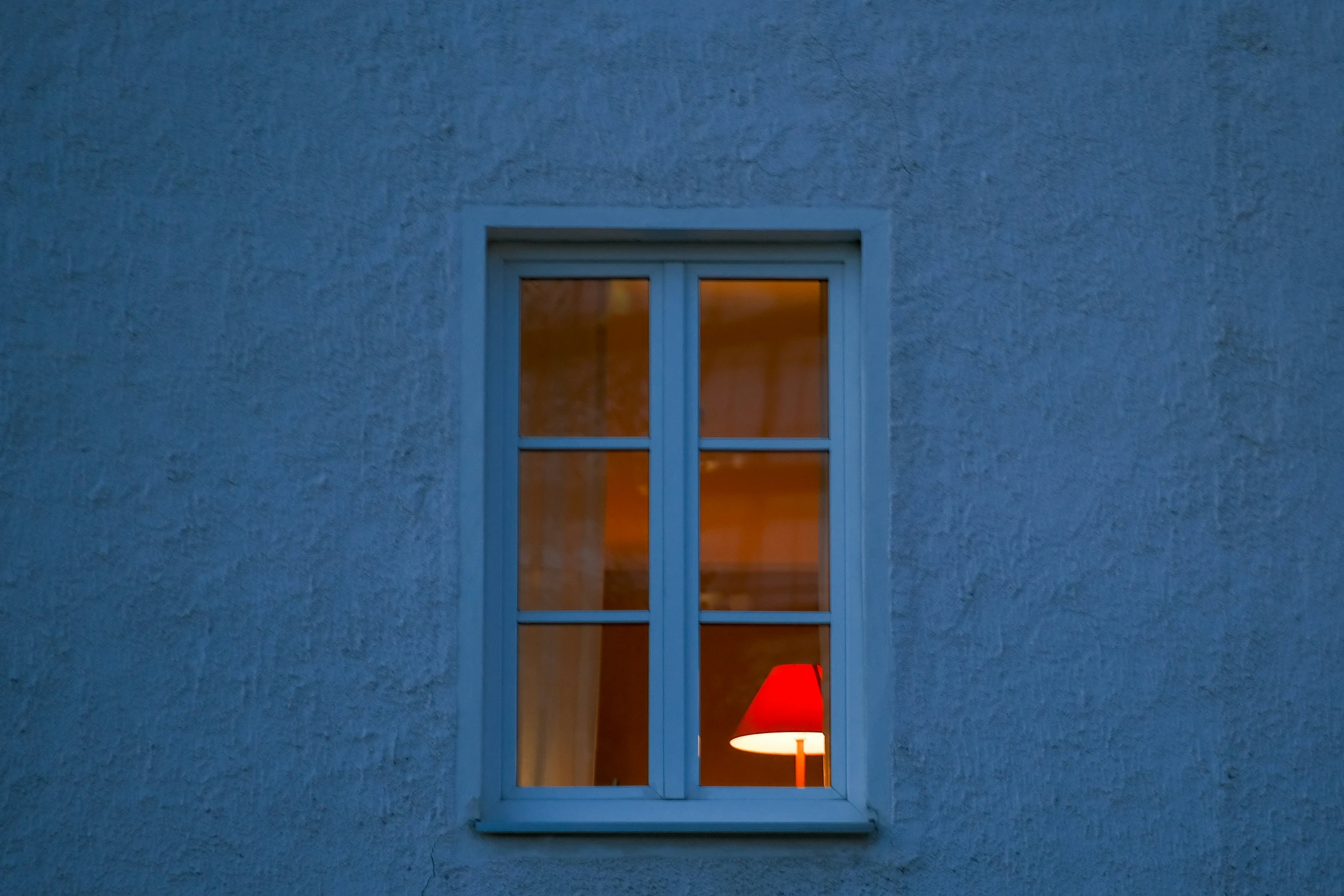 a red lamp sitting under a window next to a blue wall