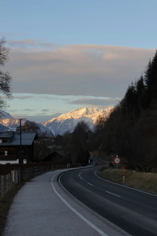 a small paved street by a road with snow covered mountains in the distance