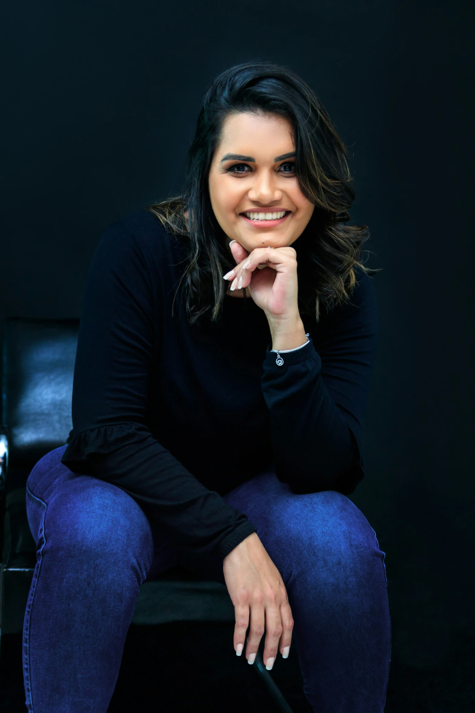 smiling woman in black top and jeans sitting on a chair