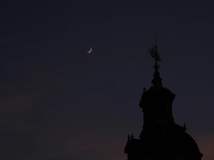 the silhouette of a tower with a clock and a crescent moon