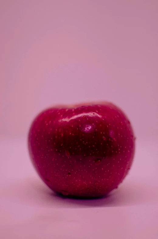 an apple on the ground in front of a pink background