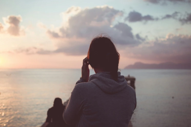 person standing on a beach near the ocean and talking on a cell phone