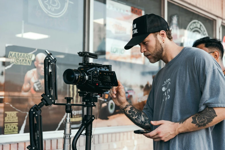 a man in gray shirt and hat standing next to camera