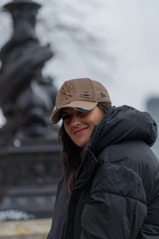 a woman standing in front of a stone fountain wearing a baseball hat