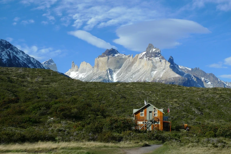 there is a small cabin in the wilderness with mountains and clouds