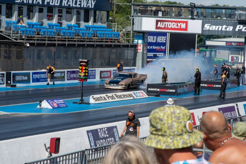 smoke is rising from a drag car while people watch