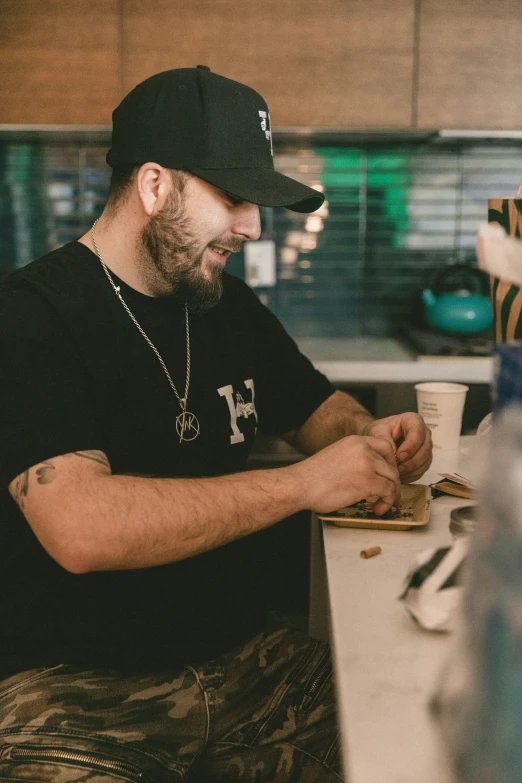 a bearded man sits in front of a counter as someone wraps his finger