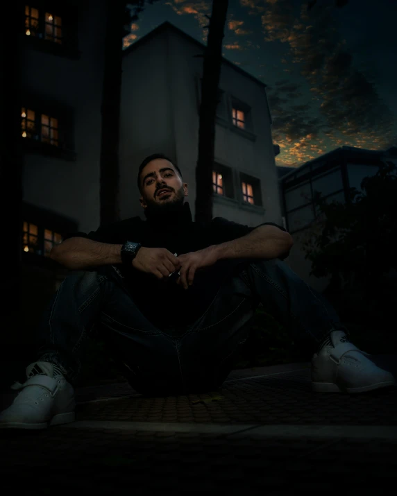 a man in black sitting on the floor with his hands folded