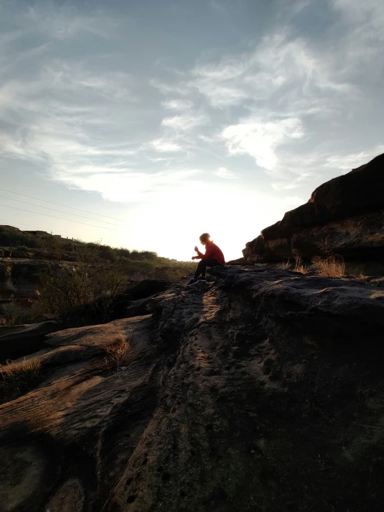 person seated on rock using cell phone while sitting