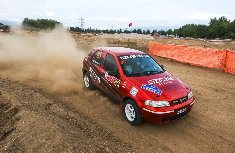 a small car driving down a dirt road near an orange barrier