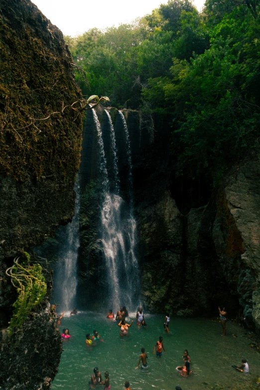 many people are standing in the water near a waterfall