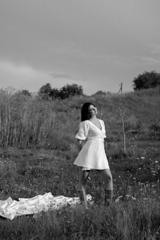 a woman poses in a field with her shirt down and a bag on the ground